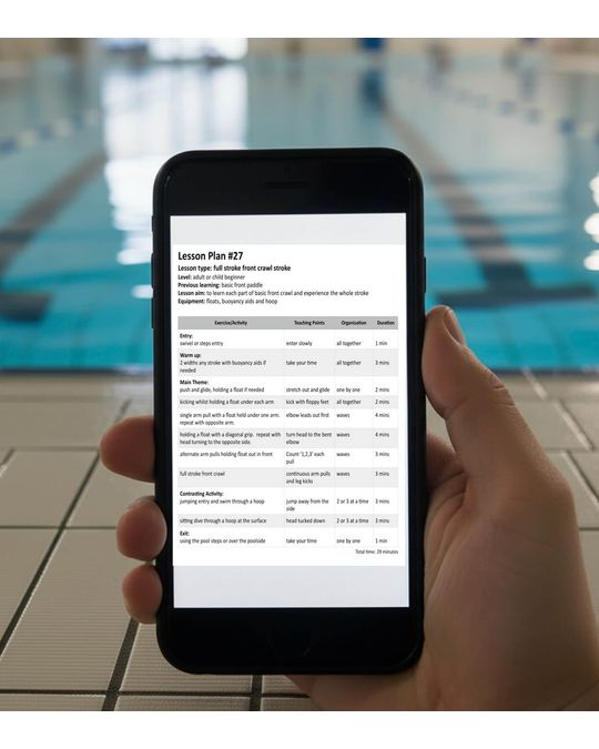 A hand holding a smartphone that displays a swimming lesson plan screen, with a blurred pool deck and water in the background.